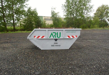 Ein weißer Bauschuttcontainer mit ARU-Logo steht auf einem Kiesplatz vor Bäumen